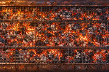 The starting grill: a rusty, dented cut oil drum seen from above, glowing charcoal under a bent wire mesh